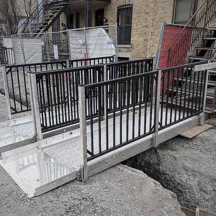 Plateforme d'accès temporaire en aluminium avec garde-corps noirs, installée sur un chantier de construction pour fournir un passage sécurisé au-dessus d'une excavation au sol.
