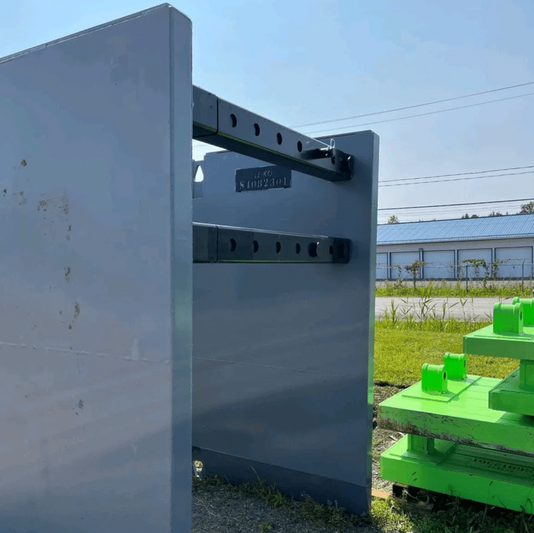 Pièce d'angle de soutènement en acier avec barres de renforcement horizontales noires, portant une plaque avec le logo et le numéro de série de Leïko Équipements, posée à côté de structures vertes sur un chantier.