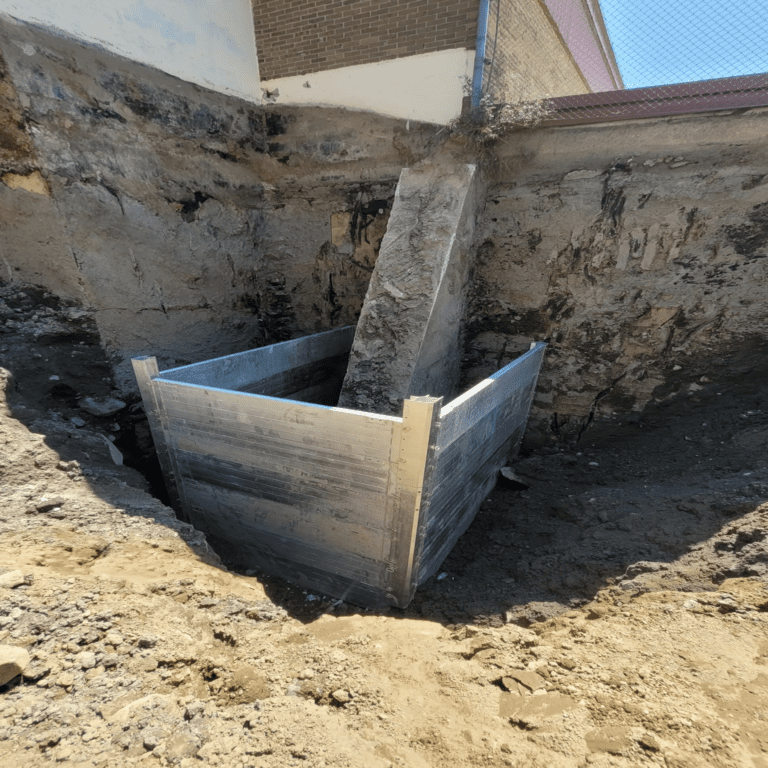 Murs de soutènement en acier installés dans une excavation profonde à côté d'un bâtiment, utilisés pour prévenir l'effondrement des terres pendant les travaux de construction ou de maintenance.