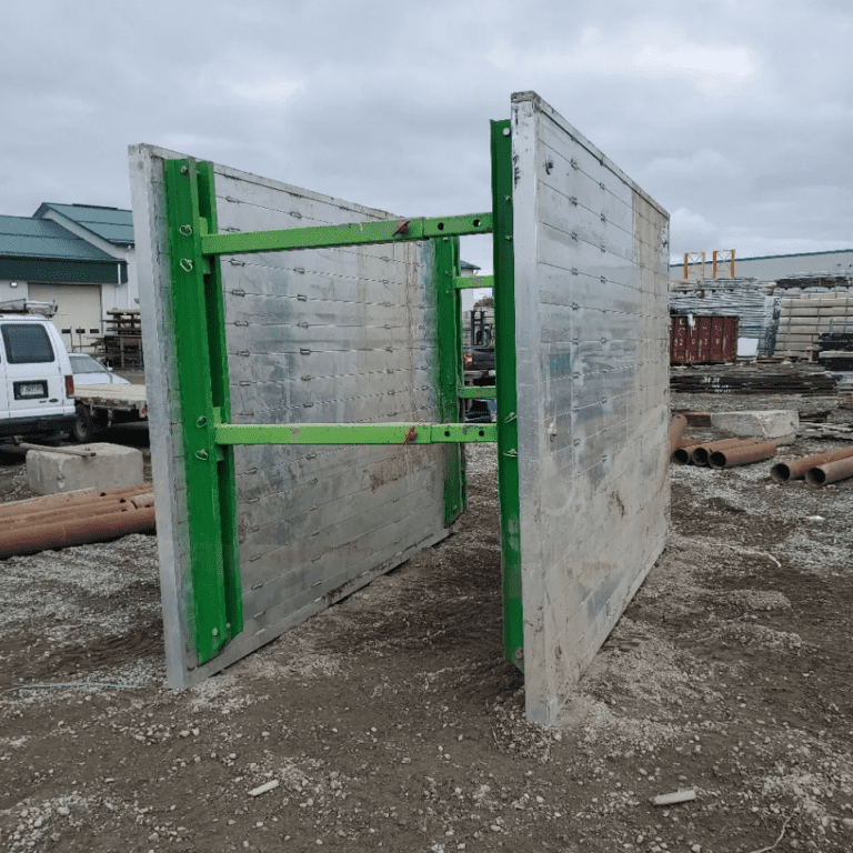 Structure de porte en acier modulaire avec panneaux métalliques et renforcements en barres vertes, assemblée sur un site de construction en extérieur.