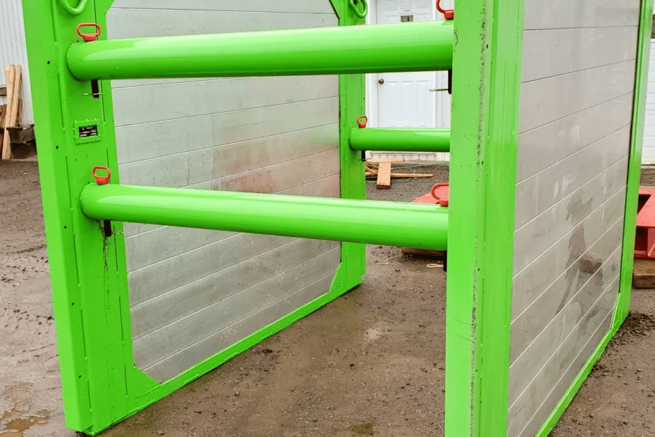 Porte de sécurité en métal bicolore avec un cadre et des barres de renforcement vert lime, sur un sol de chantier boueux, illustrant les mesures de sécurité et de contrôle d'accès dans un environnement industriel.